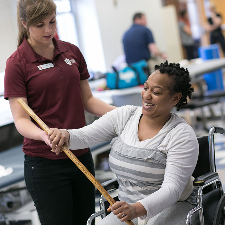 A student helping a woman in a wheelchair do excersizes.
