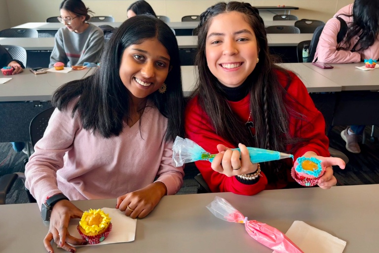 Two students pose with cupcakes and colorful bags of cake frosting.
